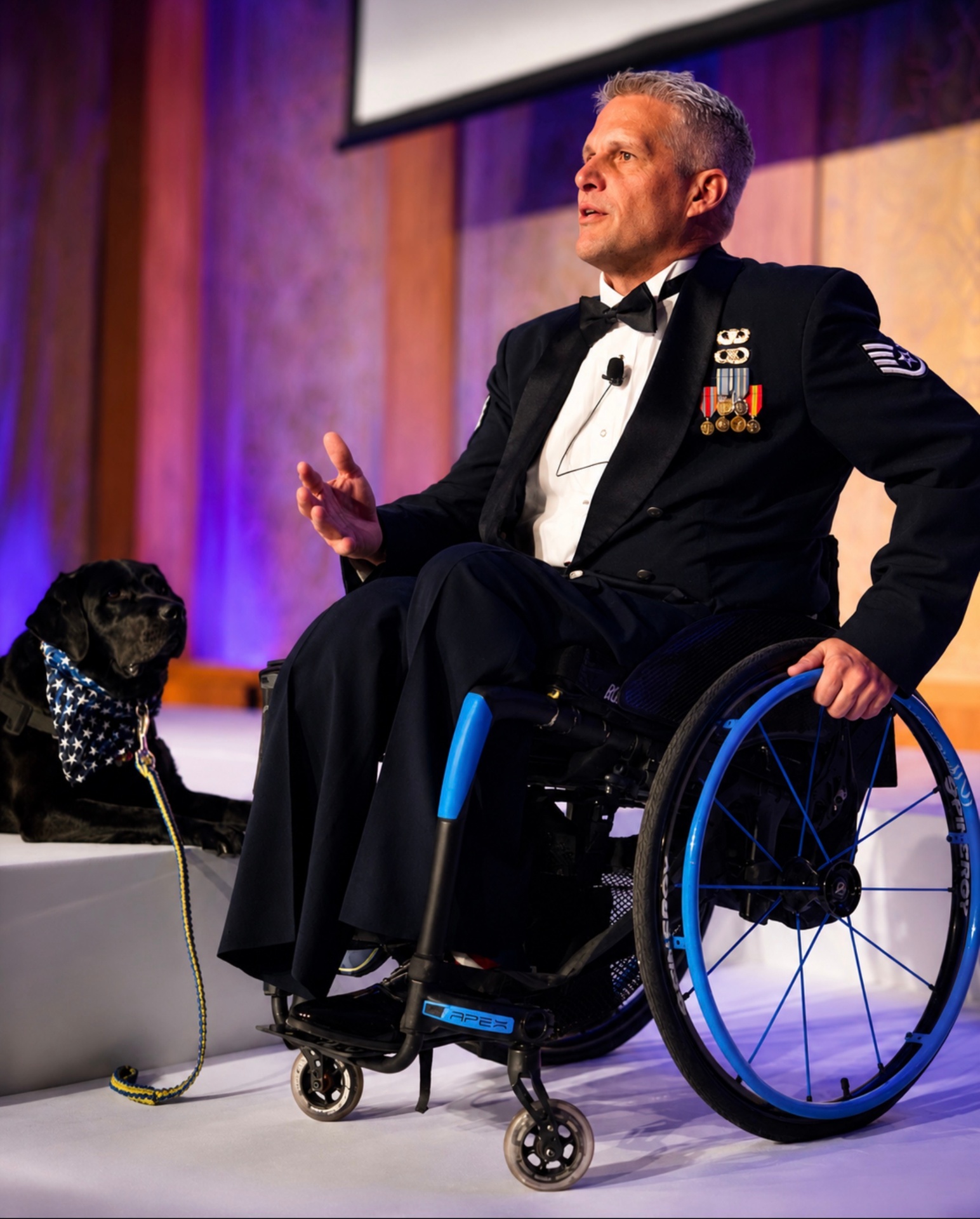 Jason Morgan speaking on stage in dress uniform with his service dog